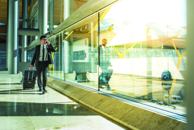 Young,businessman,walking,at,the,airport,using,his,mobile,phone